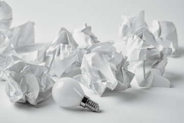 close-up shot of energy saving light bulb with crumpled papers on white