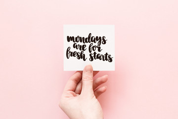 Minimal composition on a pink pastel background with girl's hand holding card with quote - Mondays are for fresh starts