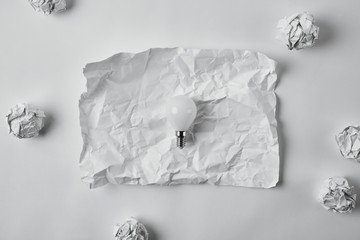 top view of power saving light bulb on crumpled blank paper on white surface