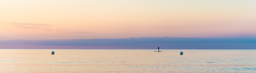 Fototapeta na wymiar panorama of a quiet scene, single man on Stand Up Paddle Board. SUP. in beatutiful sunset at the beach