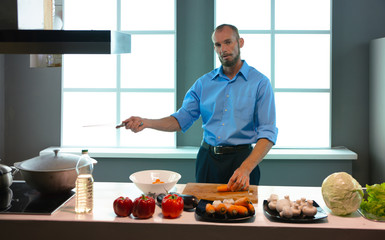A man in the kitchen is cutting carrots