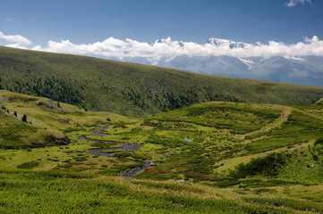 Fototapeta premium Mountain valley with green grass and ranges of hills rocks on a horizon skyline under blue sky