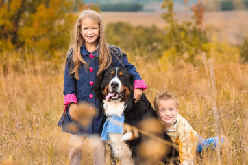 brother and his sister on walk with his four-footed dog friend on autumn meadow Berner Sennenhund