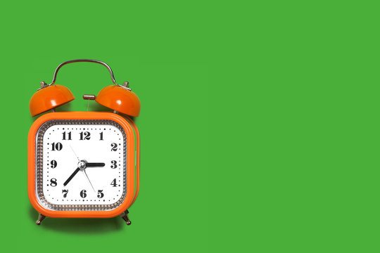 Vintage style orange metal alarm clock with bells standing on the green surface isolated. back to school concept. free space for text