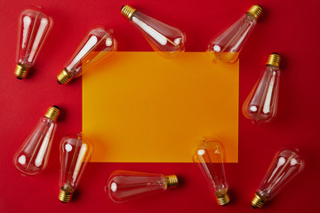 top view of vintage incandescent lamps on red surface with yellow blank paper