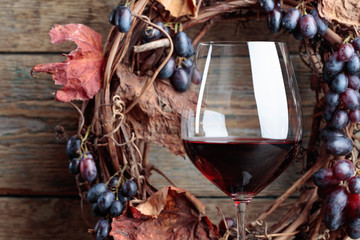 Glass of red wine with grapes and dried vine leaves.