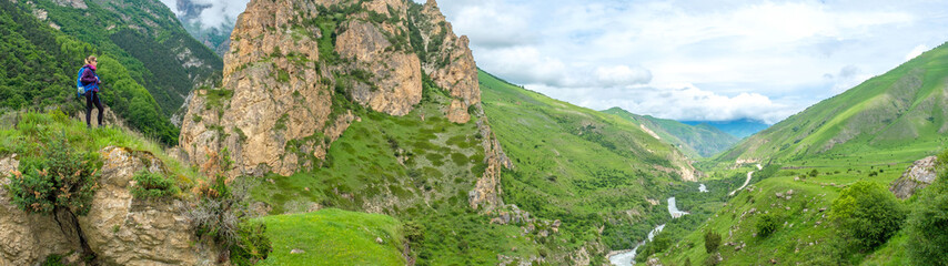 Girl with a backpack in the mountains. Trekking along the mountain road.