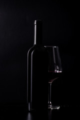 Silhouette of red wine bottle with half glass isolated on black dark background with soft reflections and beautiful shadows.