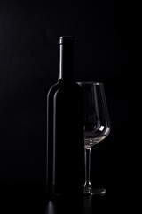 Silhouette of red wine bottle with empty half glass isolated on black dark background with soft reflections and beautiful shadows.