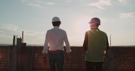 Two partners make a great deal at construction site on rooftop of building with amazing sunset