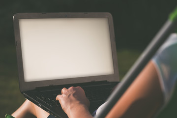 Woman is sitting in park or garden and typing on her laptop.