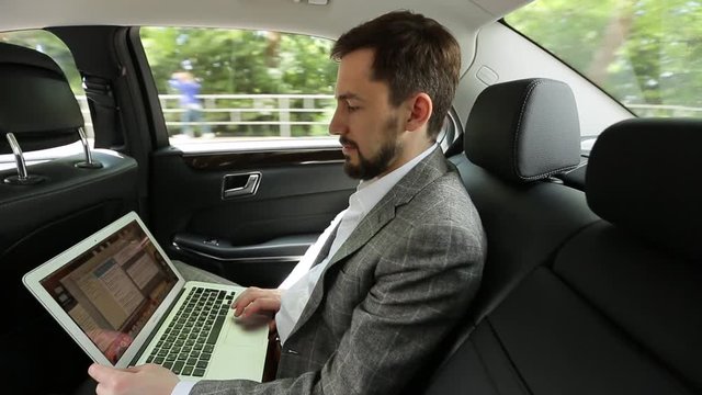 Businessman uses laptop sitting in back seat of car