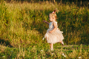 Healthy, lifestyle, happy childhood concept. Adorable little child. Girl with blonde hair, wearing a pink dress. A girl walks and run in nature in the rays of the setting sun.