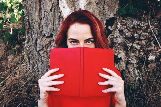 Mujer joven y pelirroja leyendo un libro al aire libre 