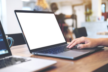 Mockup image of woman's hands using and typing on laptop with blank white desktop screen on wooden table in office