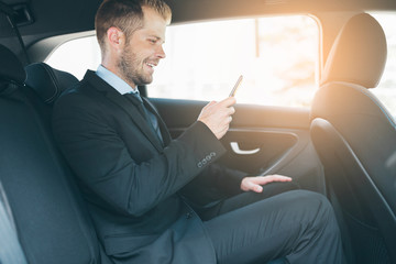 Executive businessman at the back of car using a mobile phone