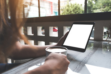 Mockup image of a woman holding black tablet pc with white blank screen while drinking coffee in cafe
