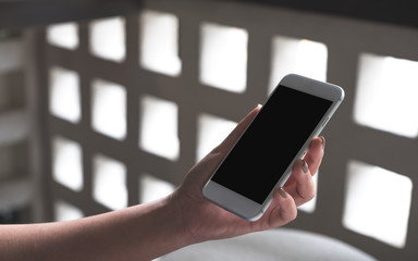 Mockup image of woman's hands holding white mobile phone with blank desktop screen in cafe