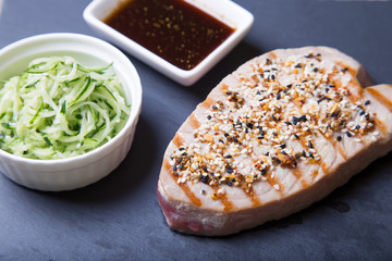 Grilled tuna with sesame and cucumber salad on a black board. Close-up, selective focus.