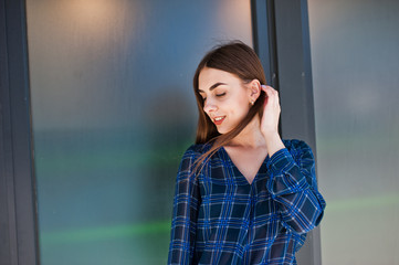 Fototapeta premium Portrait of young brunette girl in blue checkered shirt against large windows.