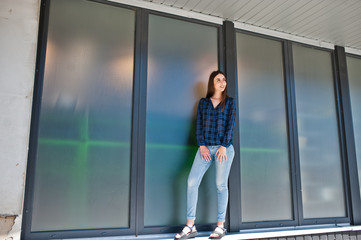 Fototapeta na wymiar Portrait of young brunette girl in blue checkered shirt against large windows.