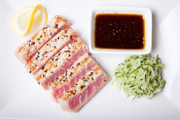 Grilled tuna with sesame seeds and cucumber salad on a white plate. Close-up, selective focus