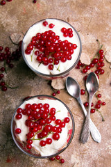 Healthy dessert with organic red currants, fresh yogurt and corn flakes. Dietary breakfast on a brown background