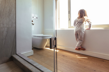 Little girl looking outside a bathroom window