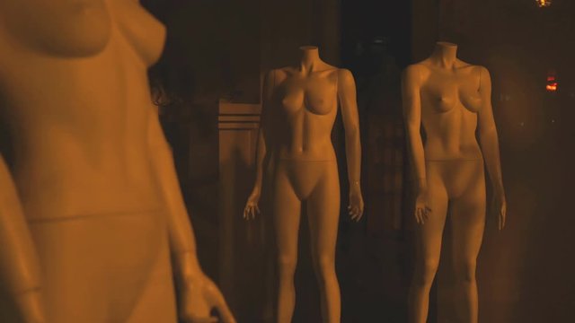 Naked stripped mannequins without clothes in hall of shop behing glass storefront
