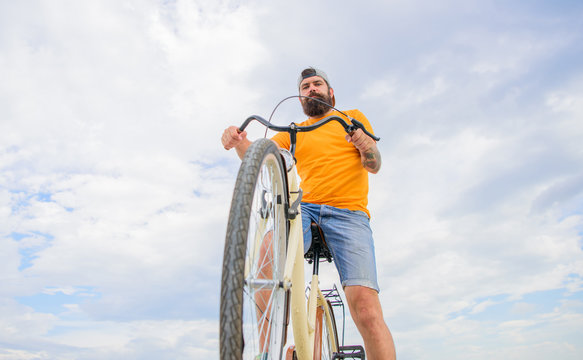 Man bearded hipster rides bicycle bottom view sky background. Modern bicycle riding culture. Optimise cycling performance. Overcome obstacles on bike. Hipster ready to perform trick
