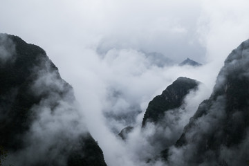 Black mystical mountains appear through thick white clouds. Mysterious gloomy landscape close-up without people