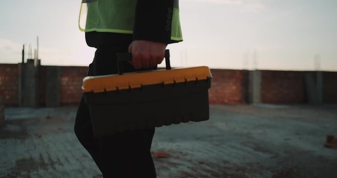 Closeup expert builder coming to his work desk putting his instrument bag on desk , he is wearing safety vest. slow motions