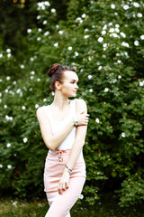 Fototapeta premium sweet cheerful girl in a white t-shirt and a pink skirt walks in the Park in the summer. She smells the flowers and enjoys the walk.