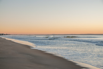A gentle early morning on the shore of the Atlantic Ocean. Surfers riding on waves in the distance. USA. Maine.

