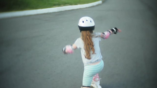 A little girl in a helmet and defense skates on roller skates. The child rolls on the rollers in the park. Girl learns to ride a roller skate.