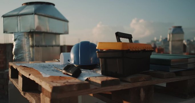 Closeup in rooftop of building , work desk with plan of construction , radio , and safety helmet.