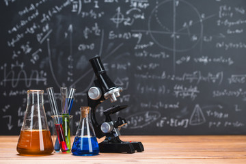 Tubes with chemical liquids stand on a wooden table on a chalkboard background