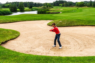 Boy golf player chipping from sand bunker onto green