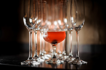 Delicious red cocktail standing among empty champagne glasses