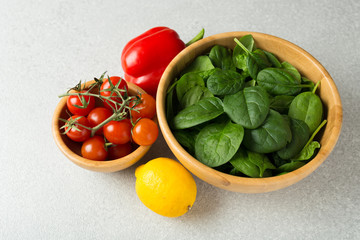Healthy food concept. Ingredients for salad. Spinach in bowl, sweet pepper, lemon, tomatoes. Top view.