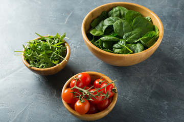 Healthy food concept. Ingredients for salad. Spinach in bowl, arugula, tomatoes. Top view.