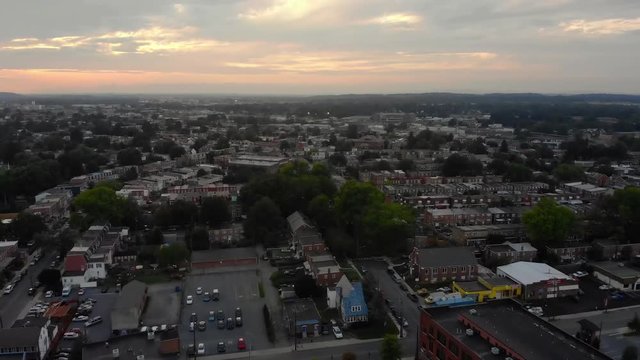 A slow aerial flyover establishing shot of a Lancaster, Pennsylvania residential district at sunset on a hazy summer evening.  	