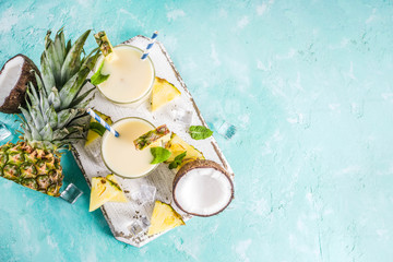 Refreshing summer drink, homemade pina colada cocktail, on a light blue background, with pieces of pineapple, coconut, ice and mint leaves, copy space top view - obrazy, fototapety, plakaty