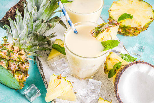 Refreshing summer drink, homemade pina colada cocktail, on a light blue background, with pieces of pineapple, coconut, ice and mint leaves, copy space top view