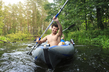 Rafting in a canoe by the river. Young guys with oars in a boat sail on the river in the summer. Active leisure rafting on the river. Young athletic man in a kayak with an oar rowing on the water.