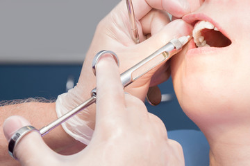 Patient visiting a dental office. Adult woman sitting in chair. Dentist hands in rubber protective gloves. Receiving anesthesia by syringe. Open mouth. Check up teeth.