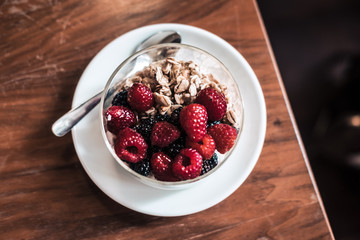 Overhead yogurt with granola, raspberries on wooden coffee table. Hipster coffee shop. Food photography concept. Image filter tones. Copyspace