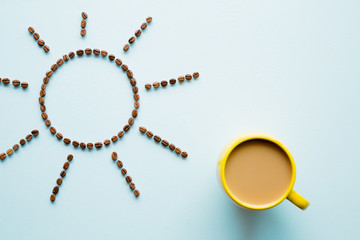 Yellow mug of coffee with milk on light pastel blue table. Wake up with morning coffee. Sun shape...