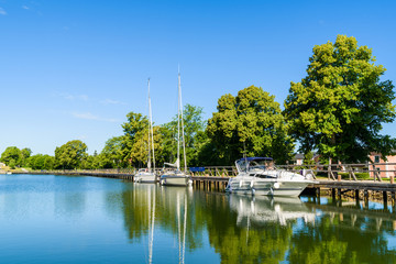 Three boats moored at a long wooden pier or promenade along Gota canal in Berg, Sweden.