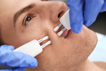 Young man undergoing microcurrent therapy in beauty salon, closeup
